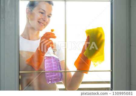 Woman in rubber gloves and apron manually washes window balcony of house with rag cleaner and mop outside behind glass. Restoring order and cleanliness in spring, cleaning servise Woman in rubber gloves and apron manually washes window balcony of house with rag cleaner and mop outside behind glass. Restoring order and cleanliness in spring, cleaning servise 130995081