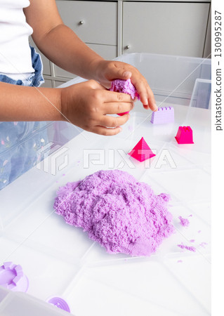 Child playing with purple kinetic sand and geometric molds Child playing with purple kinetic sand and geometric molds 130995287