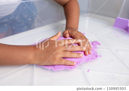Child playing with purple kinetic sand on white table 130995303