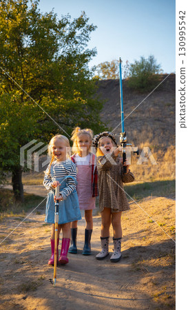 Three cheerful girls in rubber boots holding fishing rods outdoors 130995542