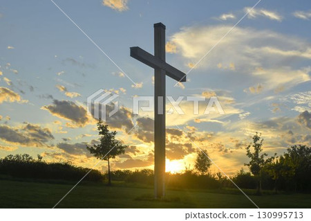 A large Christian cross in the scenery of a landscape. A Christian cross lighted by the setting sun. The concept of religion and Christianity. 130995713
