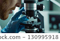 A close - up of the scientist hands - gloved hands adjust the focus of the microscope 130995918