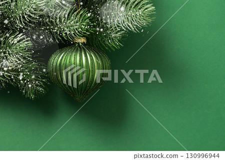 Christmas green bauble on fir snowy branch and lights garland on green background. Xmas greeting card. New Year banner. Copy space. View from above. Christmas green bauble on fir snowy branch and lights garland on green background. Xmas greeting card. New Year banner. Copy space. View from above. 130996944