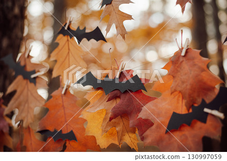 Black bats made of paper on red and yellow leaves in forest. Halloween celebrations 130997059