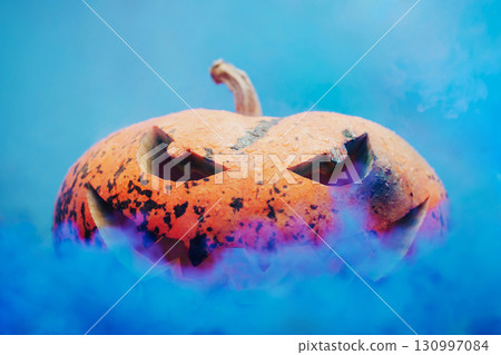 Yellow pumpkin with grinning face in blue smoke. Colorful photo of halloween pumpkin with creepy mysterious smile Yellow pumpkin with grinning face in blue smoke. Colorful photo of halloween pumpkin with creepy mysterious smile 130997084