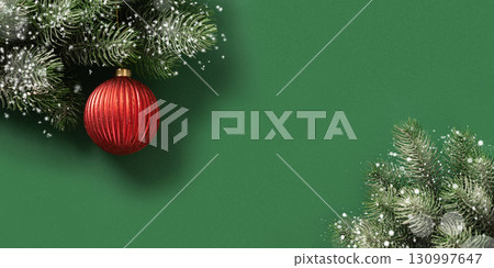 Christmas red bauble on fir snowy branches on green background. Xmas greeting card. New Year banner. Copy space. View from above. 130997647