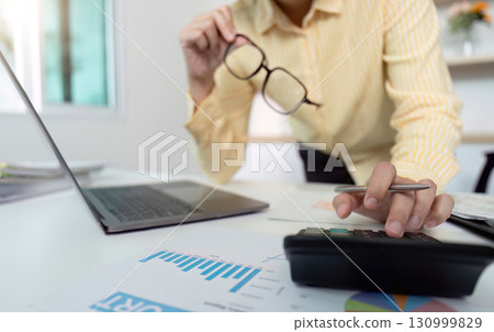 Data Review. Woman analyzing financial reports with glasses and calculator. Data Review. Woman analyzing financial reports with glasses and calculator. 130999829