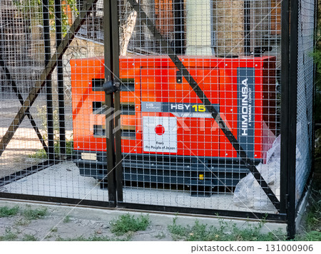 Dnipro, Ukraine - June 28, 2024: Diesel generator to support the operation of the boiler room of a residential apartment building during a power outage in cold weather. Dnipro, Ukraine - June 28, 2024: Diesel generator to support the operation of the boiler room of a residential apartment building during a power outage in cold weather. 131000906
