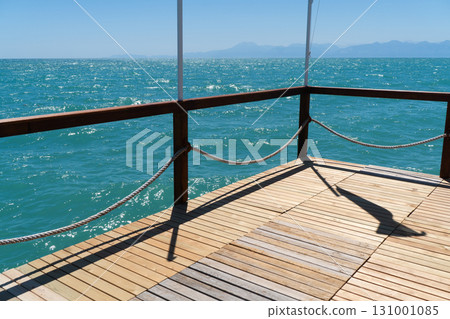 Wooden pier with posts and ropes with sparkling sea water. Wooden pier with blue sea background. 131001085