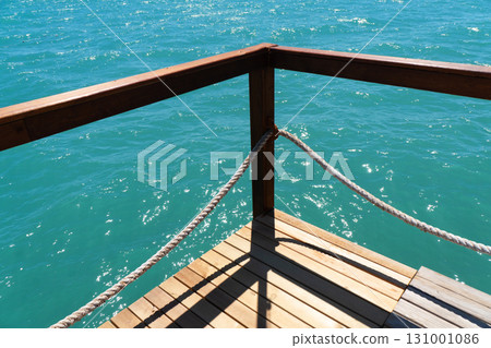 Wooden pier with posts and ropes with sparkling sea water. Wooden pier with blue sea background. Wooden pier with posts and ropes with sparkling sea water. Wooden pier with blue sea background. 131001086