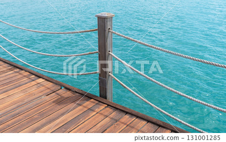 Wooden pier with posts and ropes with sparkling sea water. Wooden pier with blue sea background. 131001285
