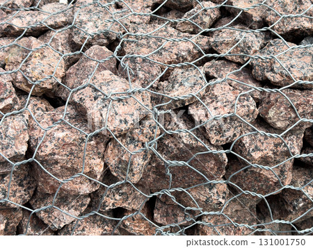Gabion wall with grey stones in a metal grid. Gray pebbles lie behind a metal grid. Fence made of stones. Decorative stones Gabion wall with grey stones in a metal grid. Gray pebbles lie behind a metal grid. Fence made of stones. Decorative stones 131001750