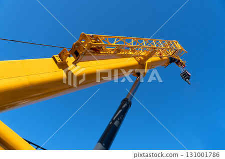Construction crane arm with hook against blue sky background. Mobile construction tower crane with telescopic boom 131001786