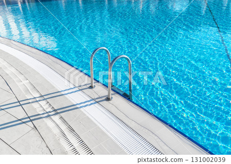 Swimming pool with stair and water. Swimming pool with handrail. Stainless steel ladder in pool. Grab bars ladder in the blue swimming pool Swimming pool with stair and water. Swimming pool with handrail. Stainless steel ladder in pool. Grab bars ladder in the blue swimming pool 131002039
