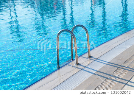 Swimming pool with stair and water. Swimming pool with handrail. Stainless steel ladder in pool. Grab bars ladder in the blue swimming pool 131002042