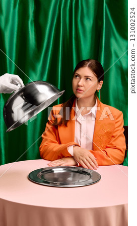 Woman in orange jacket at table with silver plate under cloche service. Negative space for ads Woman in orange jacket at table with silver plate under cloche service. Negative space for ads 131002524