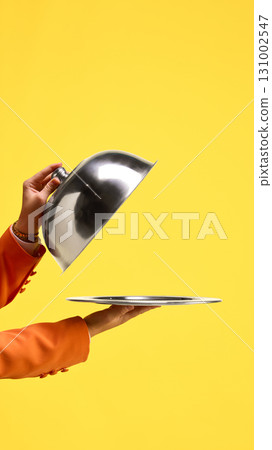 Silver cloche lifted to reveal empty tray against yellow background. Copy space for ads Silver cloche lifted to reveal empty tray against yellow background. Copy space for ads 131002547