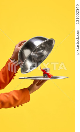 Silver cloche reveals roll of money with red ribbon on tray against yellow background Silver cloche reveals roll of money with red ribbon on tray against yellow background 131002549