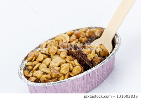 Caramel toffee cake topped with roasted peanut in pink foil container, partly eaten with wooden fork, sweet dessert, isolated on white background Caramel toffee cake topped with roasted peanut in pink foil container, partly eaten with wooden fork, sweet dessert, isolated on white background 131002839