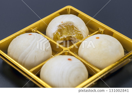 Chinese mooncakes filled with bean paste, one with bite taken, displayed on golden tray, showcasing traditional dessert with soft texture and sweet flavor 131002841