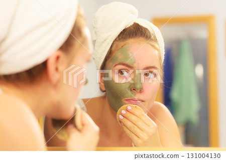 Woman removing facial clay mud mask in bathroom Woman removing facial clay mud mask in bathroom 131004130