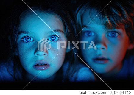 Two children watching glowing screen in dark room 131004140