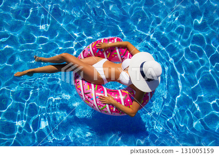 Beautiful brunette woman sits on an pink inflatable ring at swimming pool 131005159