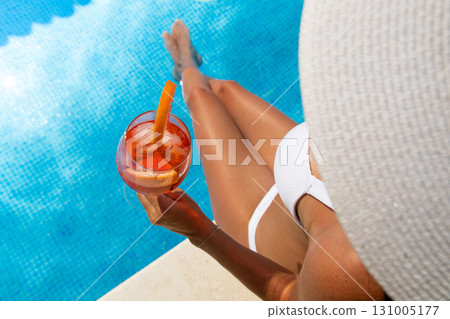 Beautiful brunette woman in a hat sitting and enjoying cocktail at swimming pool Beautiful brunette woman in a hat sitting and enjoying cocktail at swimming pool 131005177