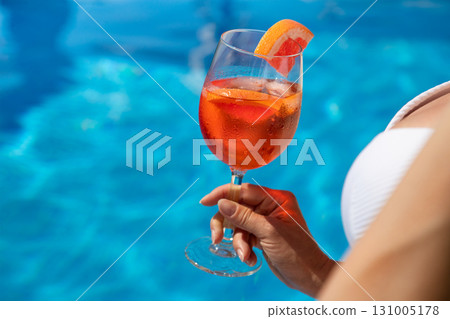 Beautiful brunette woman in a hat sitting and enjoying cocktail at swimming pool 131005178