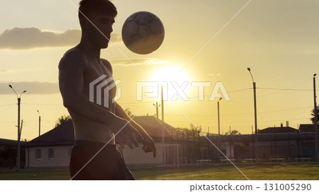 Young man juggling soccer ball on stadium at sunset. Professional footballer kicking ball at green field. Sportsman practicing tricks at meadow with sunlight at background. Freestyle football Young man juggling soccer ball on stadium at sunset. Professional footballer kicking ball at green field. Sportsman practicing tricks at meadow with sunlight at background. Freestyle football 131005290