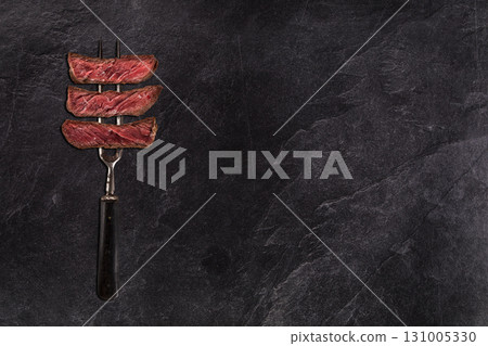 Beef rump steak on fork, black stone table, close-up. Beef rump steak on fork, black stone table, close-up. 131005330