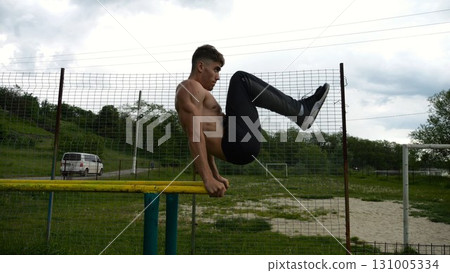 Strong guy training abdominal muscles on parallel bars at sports ground. Young shirtless sportsman exercising at nature. Sporty athlete working out at nature. Concept of active sportive lifestyle 131005334