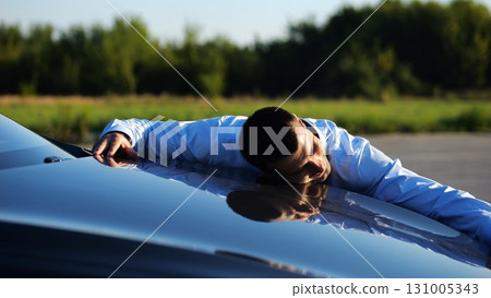 Successful smiling manager bought new electrical vehicle and hugging hood of auto. Happy young businessman in shirt enjoying modern electric automobile. Concept of buy or rent car. Slow motion 131005343