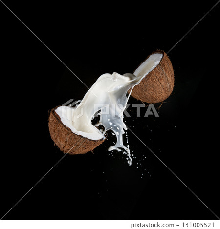 Cracked Coconut with milk splash flying in the air, isolated on black. Cracked Coconut with milk splash flying in the air, isolated on black. 131005521