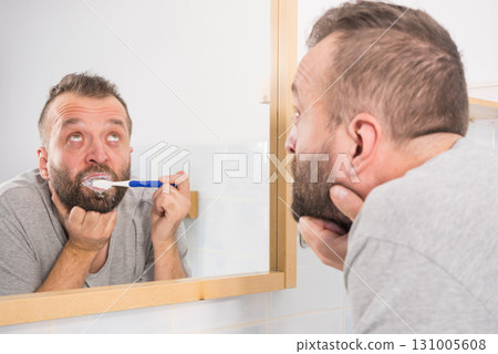 Bored guy brushing his teeth in bathroom Bored guy brushing his teeth in bathroom 131005608