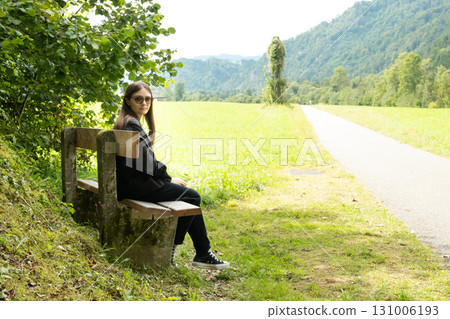 Teenage girl sitting on a bench in nature, Alps and meadows of Europe 131006193