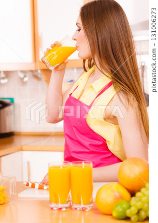 Woman in kitchen drinking fresh orange juice 131006273