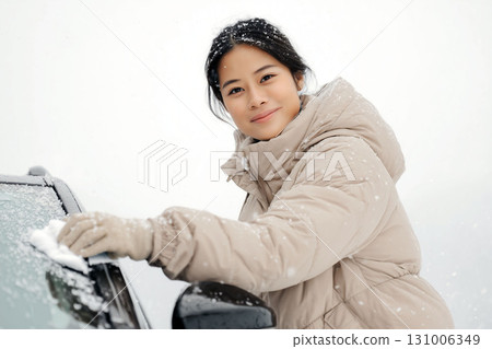 Young woman cleaning snow from car windshield on a cold winter day in snowy weather Young woman cleaning snow from car windshield on a cold winter day in snowy weather 131006349