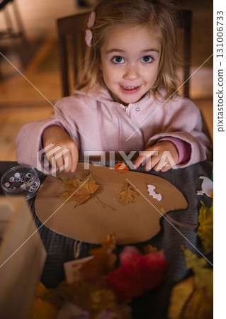 Young girl creating art with leaves and paper during indoor activity on a cozy afternoon Young girl creating art with leaves and paper during indoor activity on a cozy afternoon 131006733