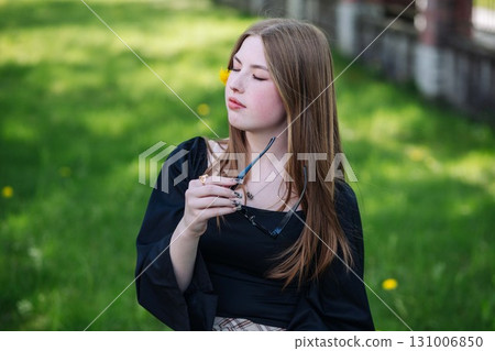High school student relaxing in a park during spring break, holding sunglasses and with a dandelion on her cheek 131006850