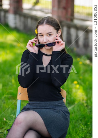 Teenage girl with dandelion in hair adjusting sunglasses while seated in schoolyard during the day Teenage girl with dandelion in hair adjusting sunglasses while seated in schoolyard during the day 131006852