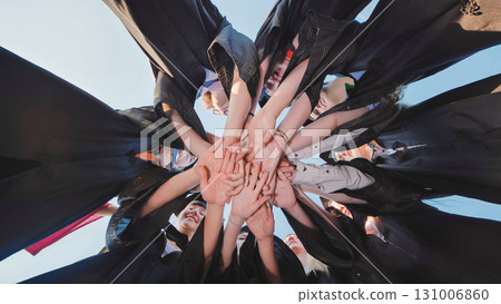 Group of students in graduation gowns link hands to celebrate their achievement in a circle 131006860