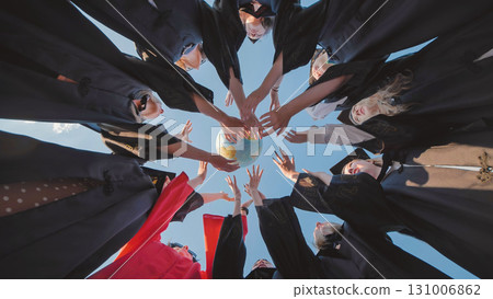 Group of graduates in academic gowns forming a circle, holding a globe, symbolizing global education and future opportunities 131006862