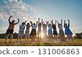 Students raising their hands at sunset in a field, celebrating their friendship and academic achievements 131006863