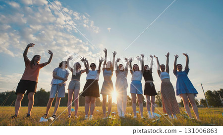 Students raising their hands at sunset in a field, celebrating their friendship and academic achievements 131006863