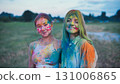 Two female school friends, covered in vibrant holi powder paint, embrace and smile during the colorful festivities 131006865
