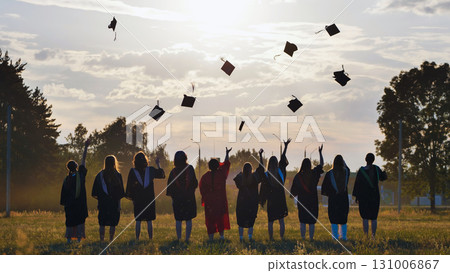 Group of graduates throwing mortarboards in the air at sunset, celebrating their academic achievement and the end of their studies 131006867