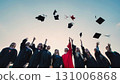 Group of cheerful graduates celebrating their academic achievement by tossing their graduation caps into the air against a sunset sky 131006868