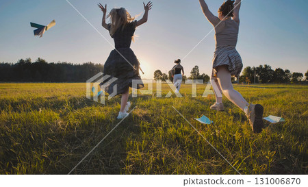 High school girls having fun running in a field at sunset, tossing paper airplanes during their summer break 131006870