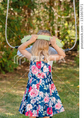 Little girl holding swing ropes and enjoying sunny day outdoors. Happy childhood, innocence and freedom. Perfect for concepts of kids activity or family life Little girl holding swing ropes and enjoying sunny day outdoors. Happy childhood, innocence and freedom. Perfect for concepts of kids activity or family life 131007071